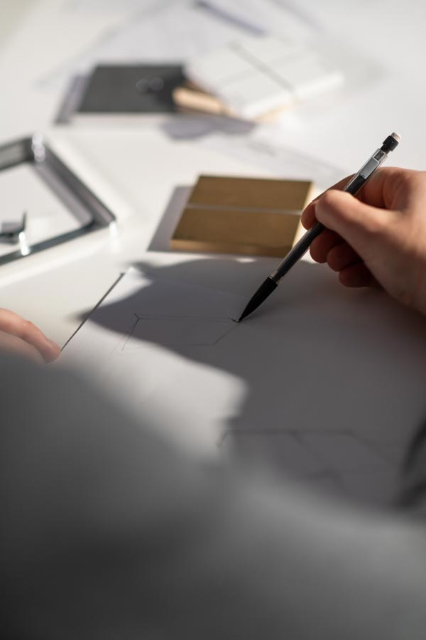 Person sketching design plans on paper with architectural tools, emphasizing creative media designs for technology integration.